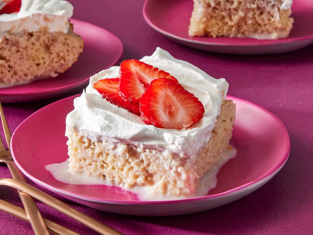 Slices of strawberry tres leches cake garnished with sliced strawberries on a pink plates