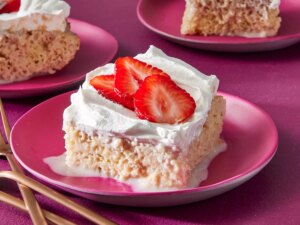 Slices of strawberry tres leches cake garnished with sliced strawberries on a pink plates