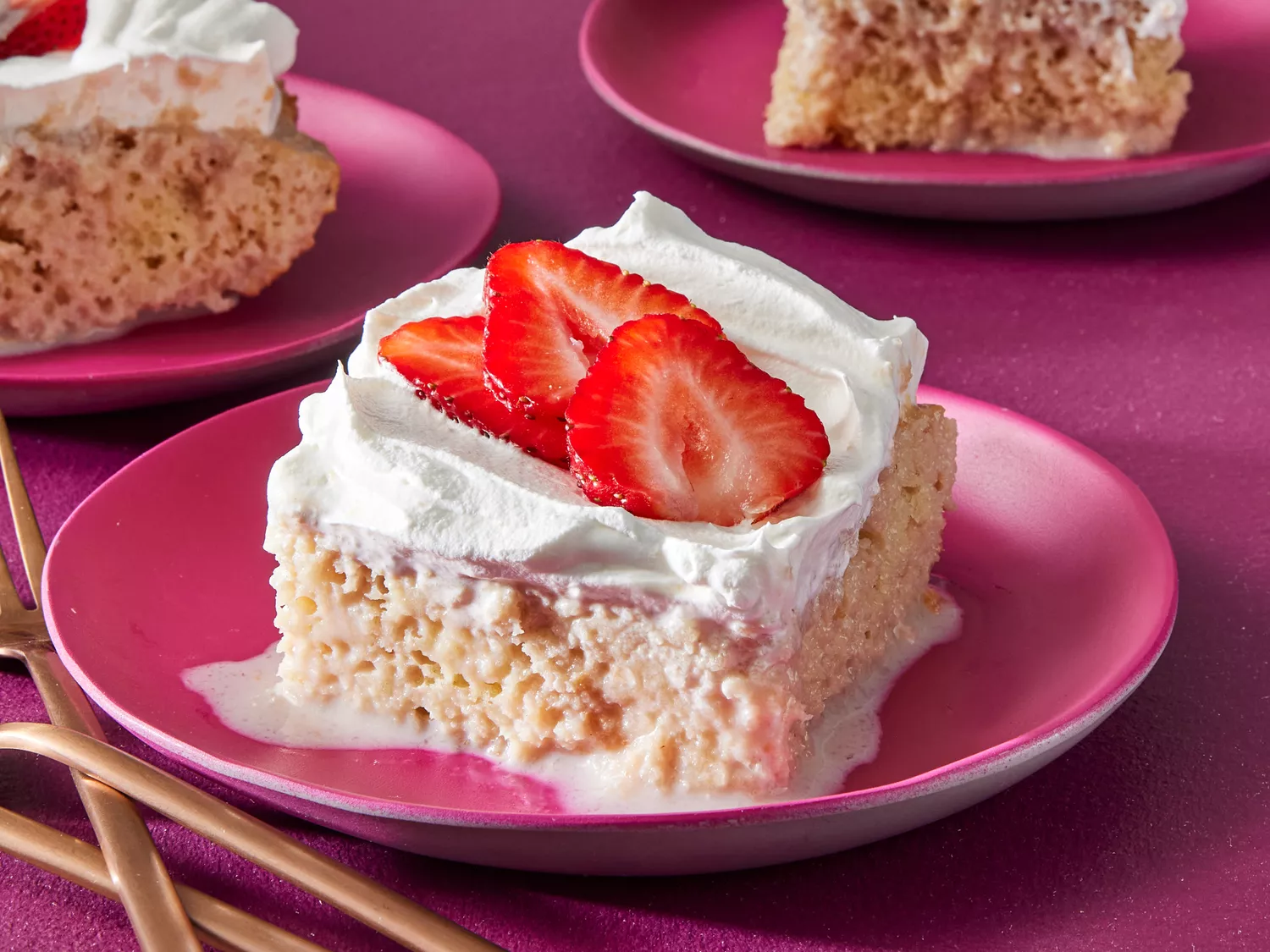 Slices of strawberry tres leches cake garnished with sliced strawberries on a pink plates