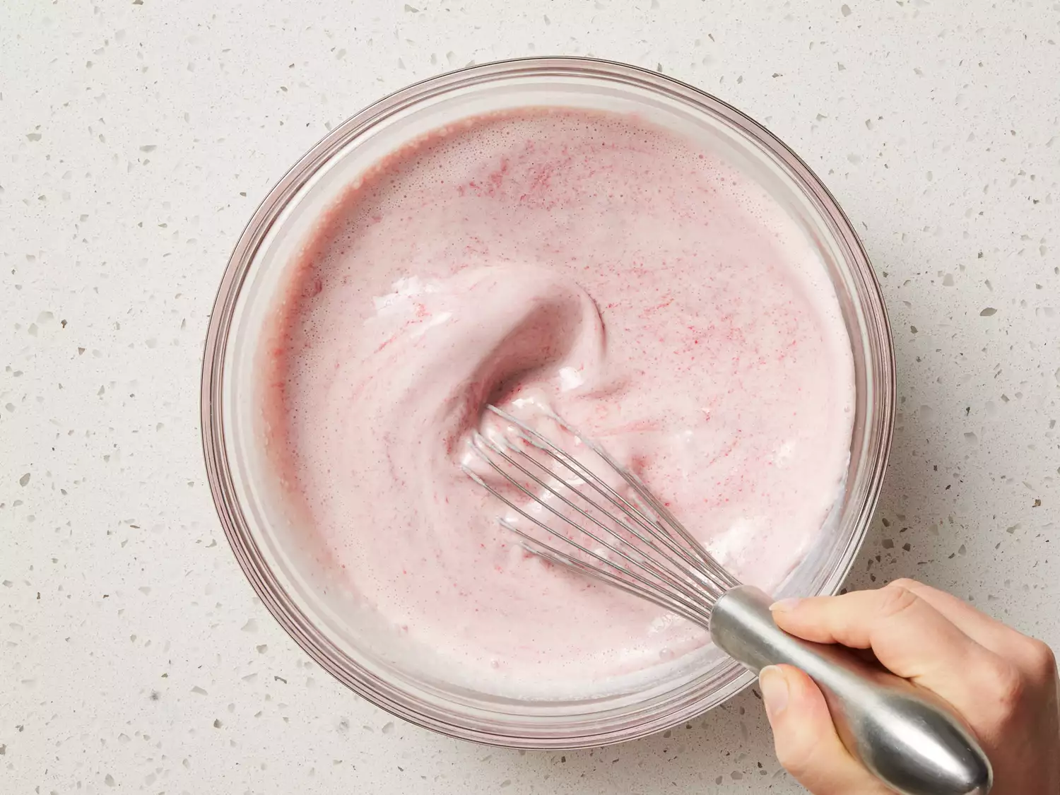 Hand whisking strawberry milk in a glass bowl 