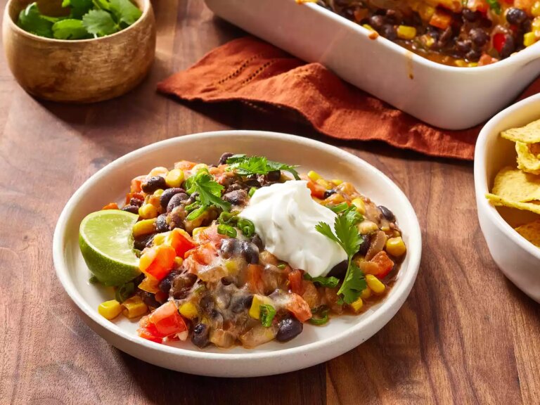 Black bean casserole garnished with cilantro, a lime wedge and sour cream on a plate