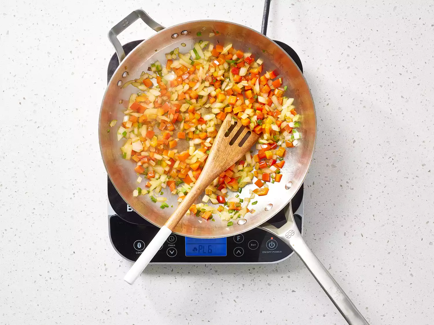 Onions and peppers cooking in a pan on a burner with a wooden spatula 