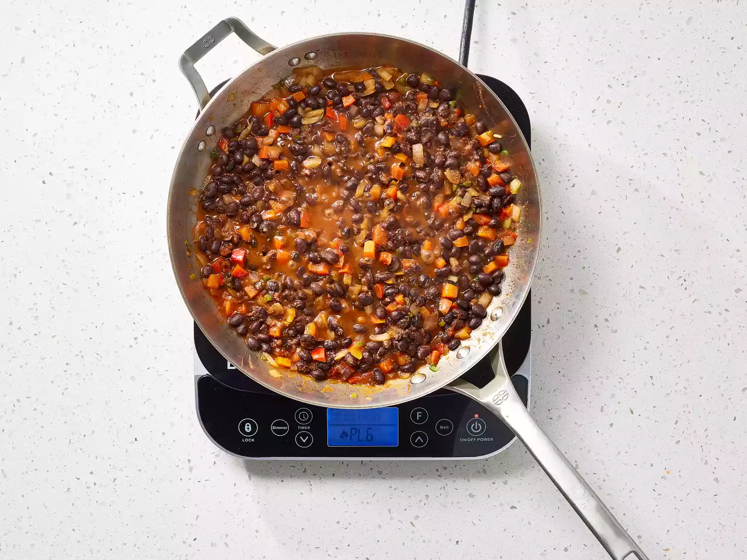 Onions, peppers and beans cooking in a pan on a burner 