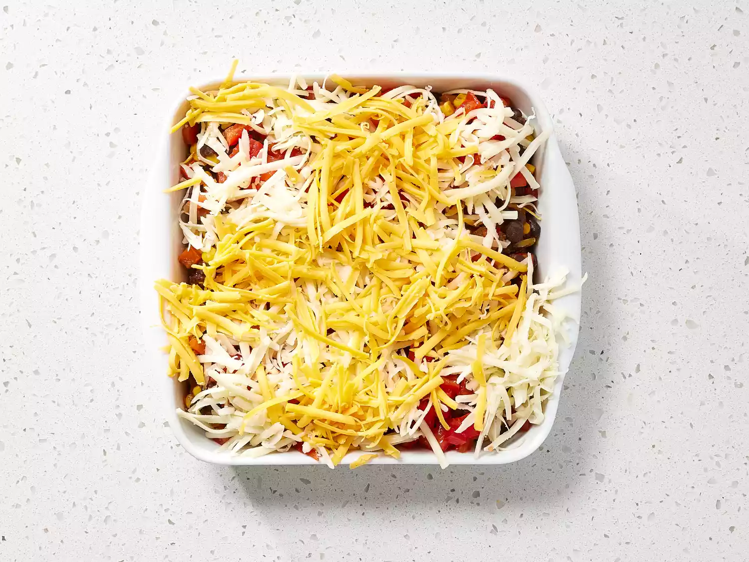 Black Bean Casserole topped with shredded cheese in a white casserole dish 