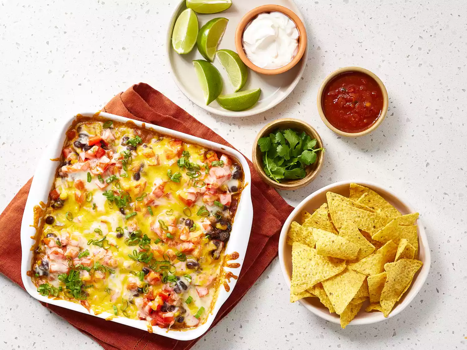 Black Bean Casserole in a white casserole dish next to chips, cilantro, salsa and lime wedges in bowls 