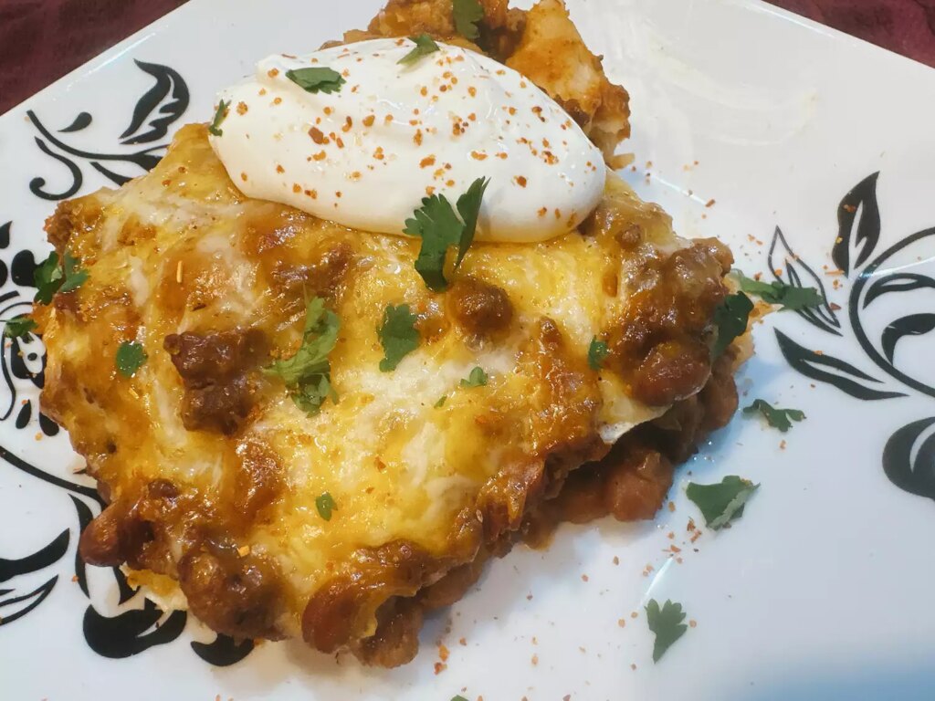 Enchilada casserole served on plate with cilantro and sour cream