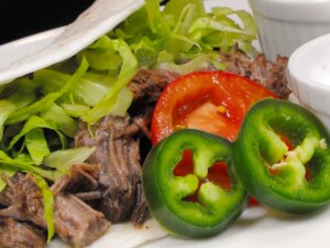 Close up view of a beef machaca taco with lettuce, tomato and jalapeno on a plate