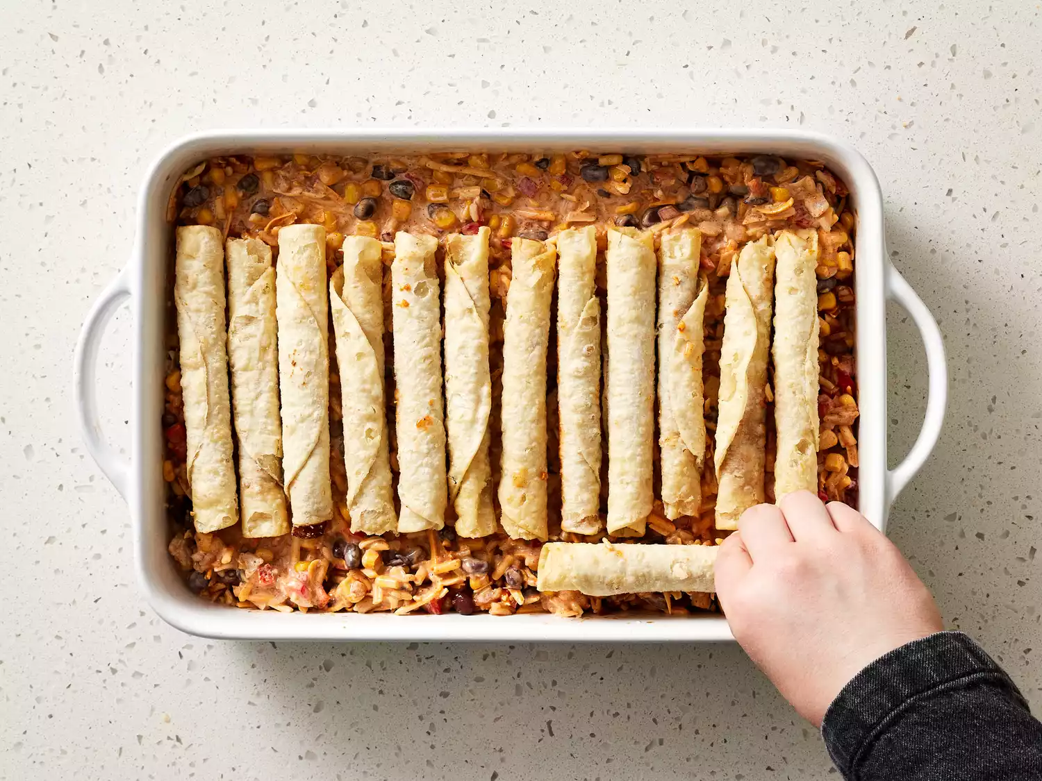 Taquito placed on top of the cheese and vegetable in a baking dish 