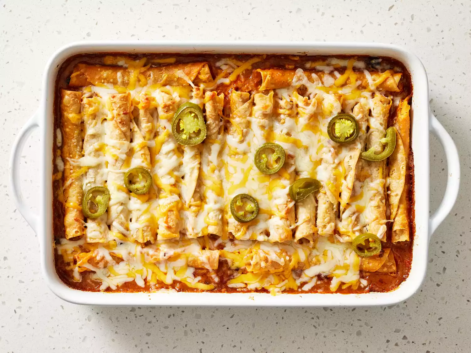 Taquito Casserole with melted cheese and pickled jalapeÃ±os on top in a baking dish 