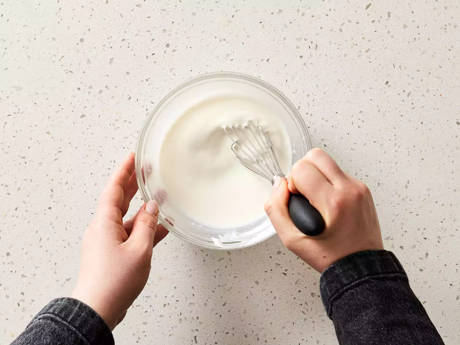 Hands whisking jalapeÃ±o crema in a glass bowl 