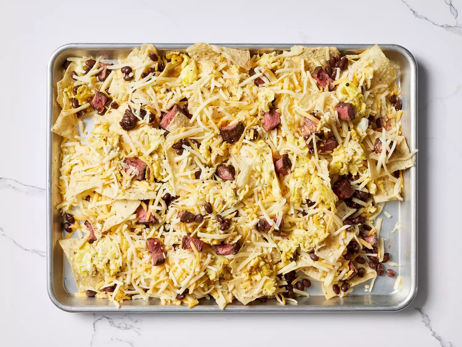 Chips covered with cheese and steak pieces on a baking sheet 