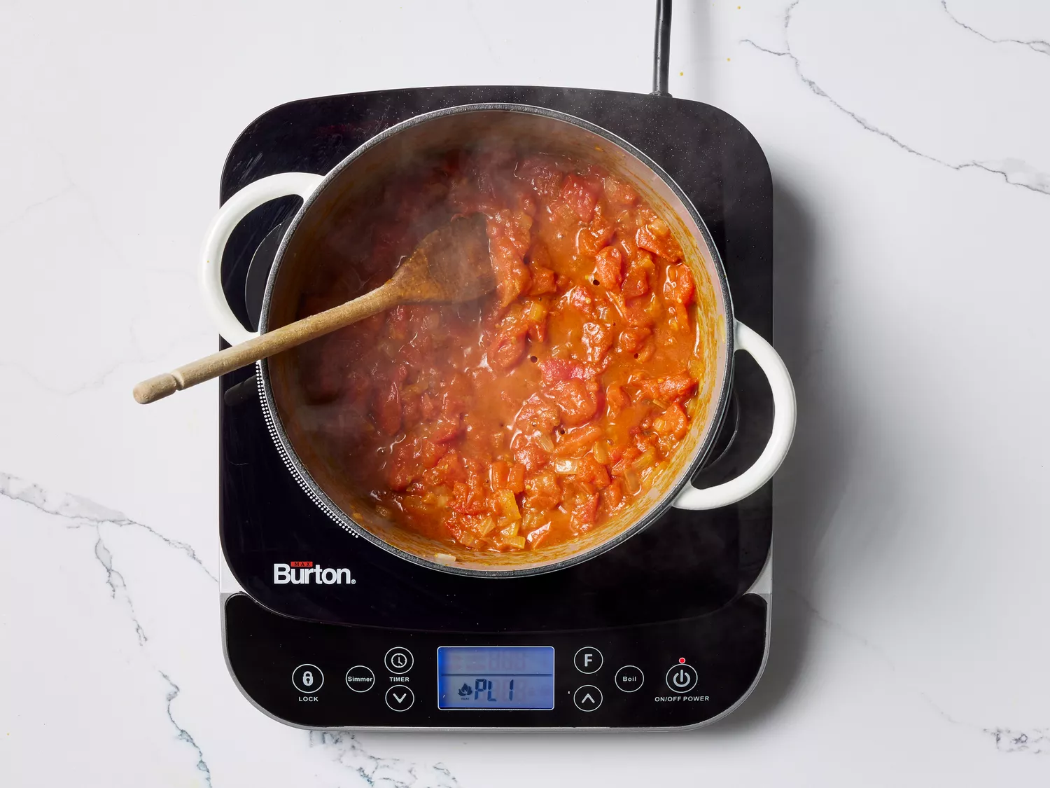 Tomato mixture in a pot with a wooden spoon on a burner 