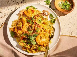 Shrimp biryani garnished with fresh herbs and fried onions on a plate with a fork