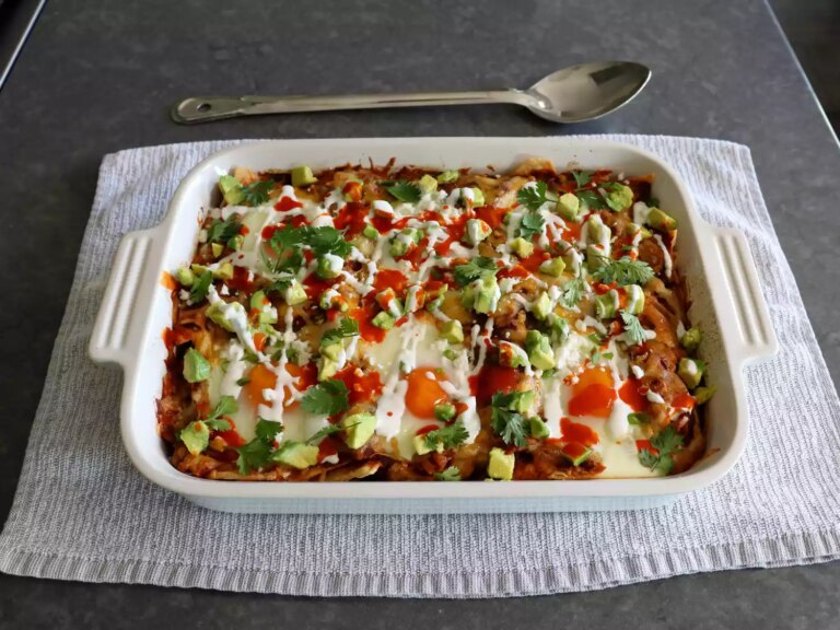 White rectangular casserole dish of chilaquiles with eggs on top, avocado, sour cream, and green onion