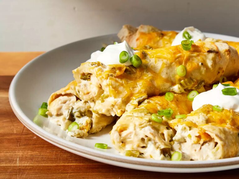 Low angle, looking at a plate of chicken enchiladas, topped with sour cream and green onions.