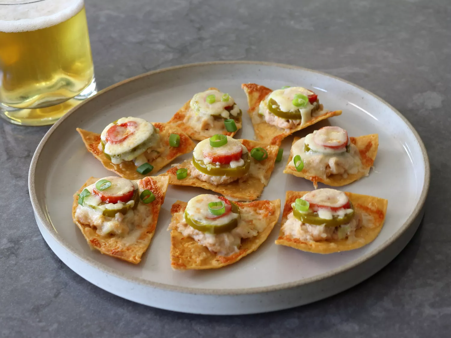 Tuna melt nachos on white plate with a beer on the side