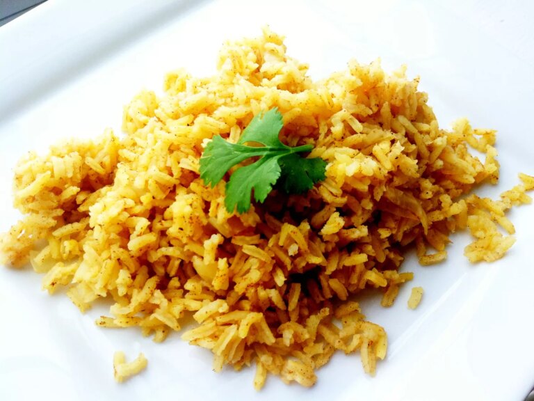 Close up view of indian rice pilaf garnished with fresh herbs on a white plate