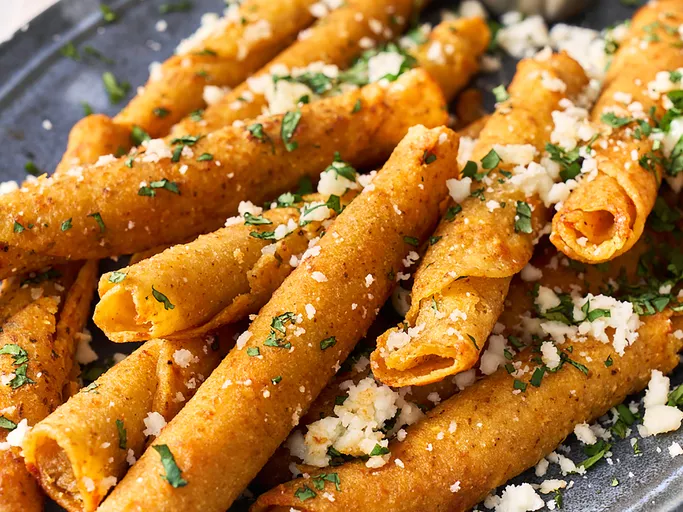 Taquitos on platter with crumbled cotija and cilantro