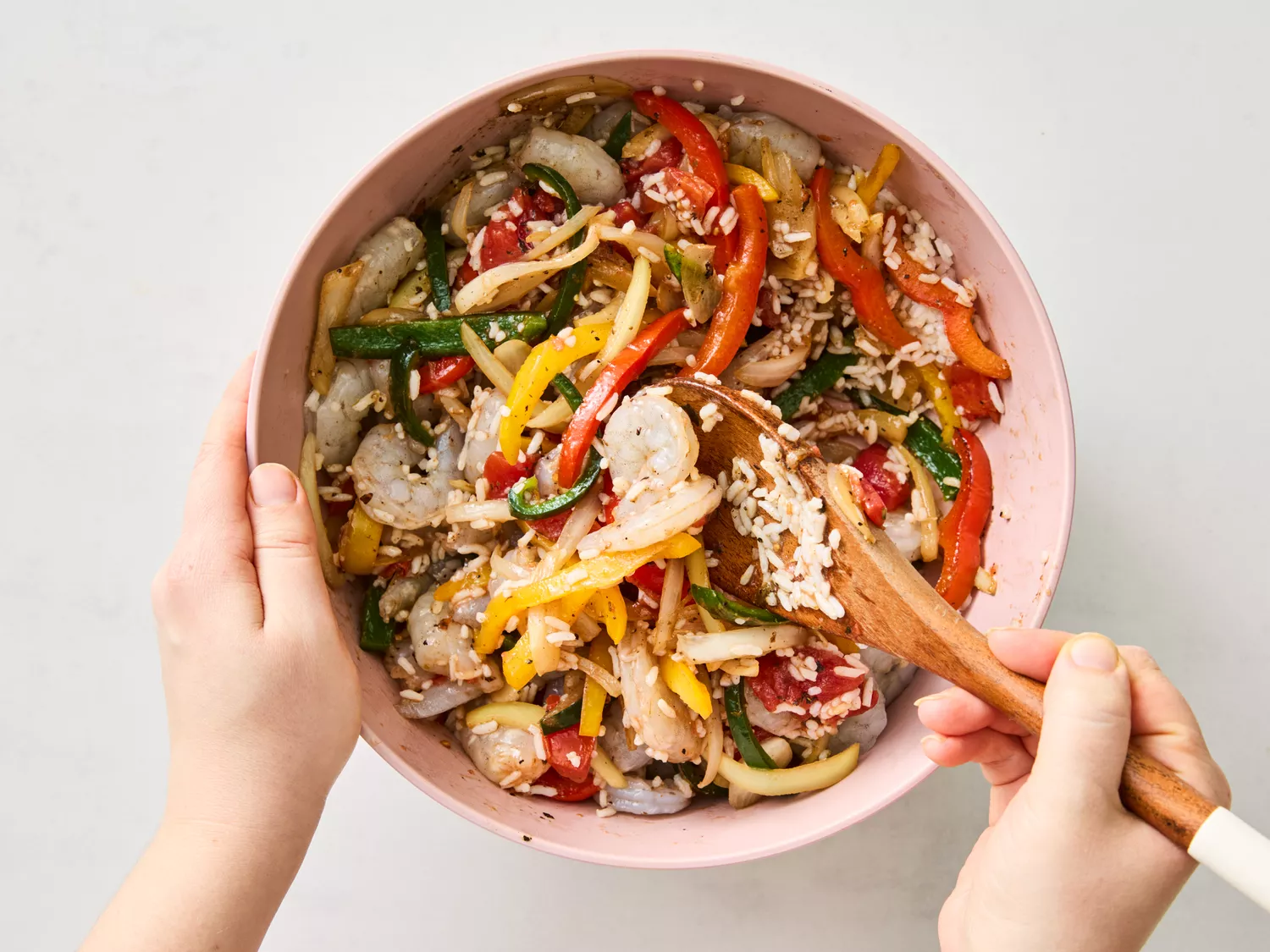 Mixing shrimp, rice, and vegetables in a pink bowl