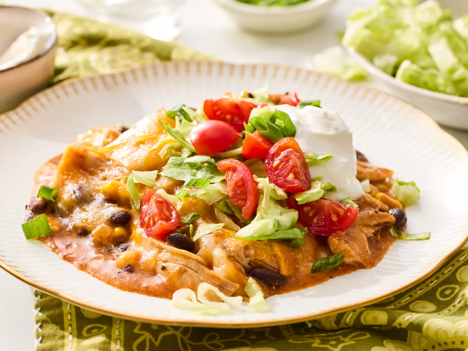 Slow cooker chicken enchilada casserole topped with sour cream, lettuce, and tomatoes in a bowl