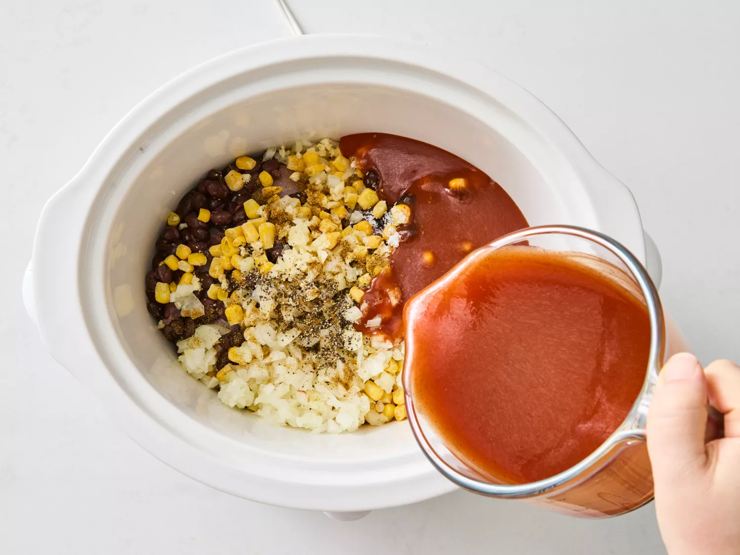 Black beans, corn, onions, and enchilada sauce being added to slow cooker