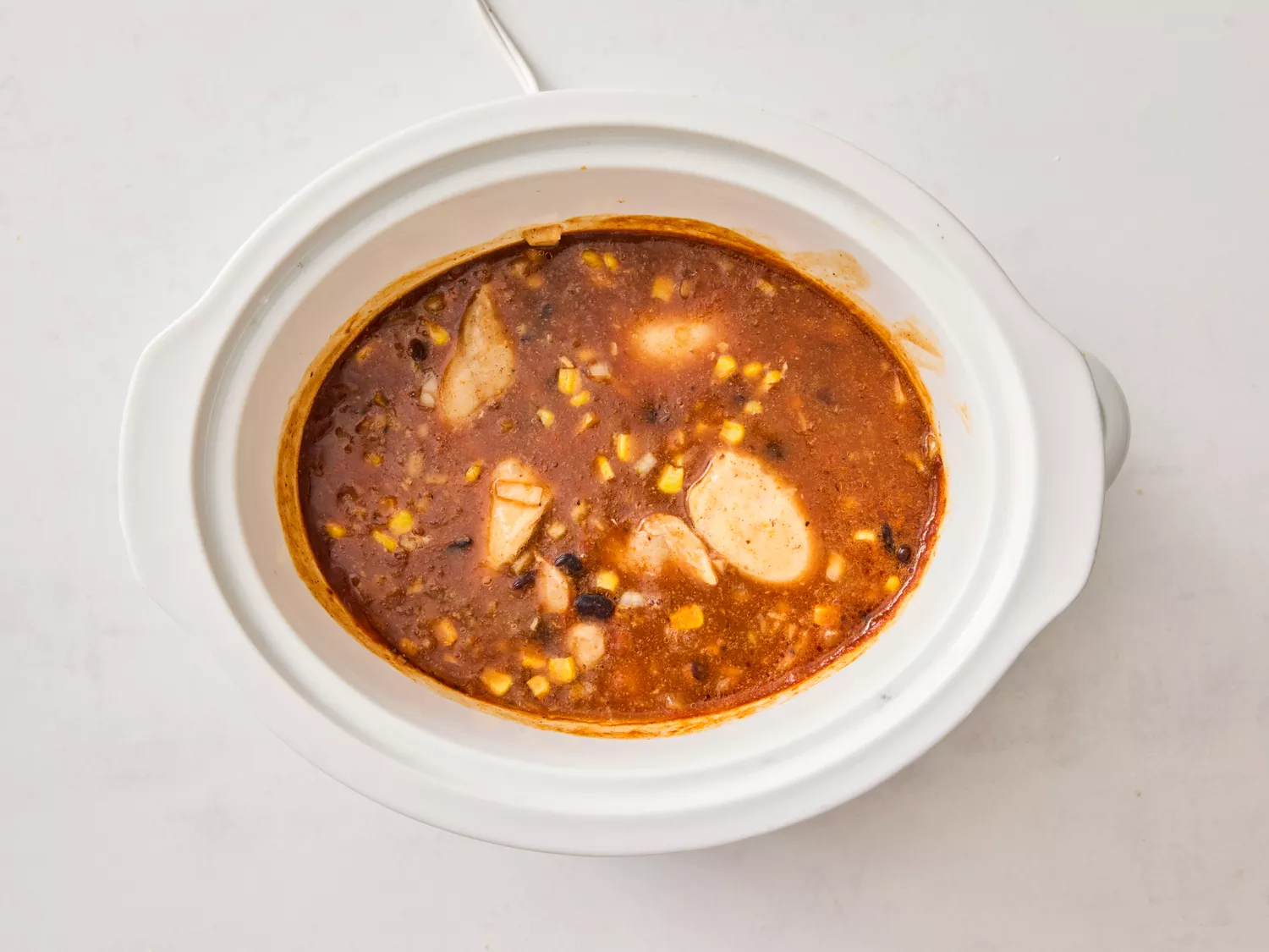 Chicken, beans, and enchilada sauce cooking in a slow cooker