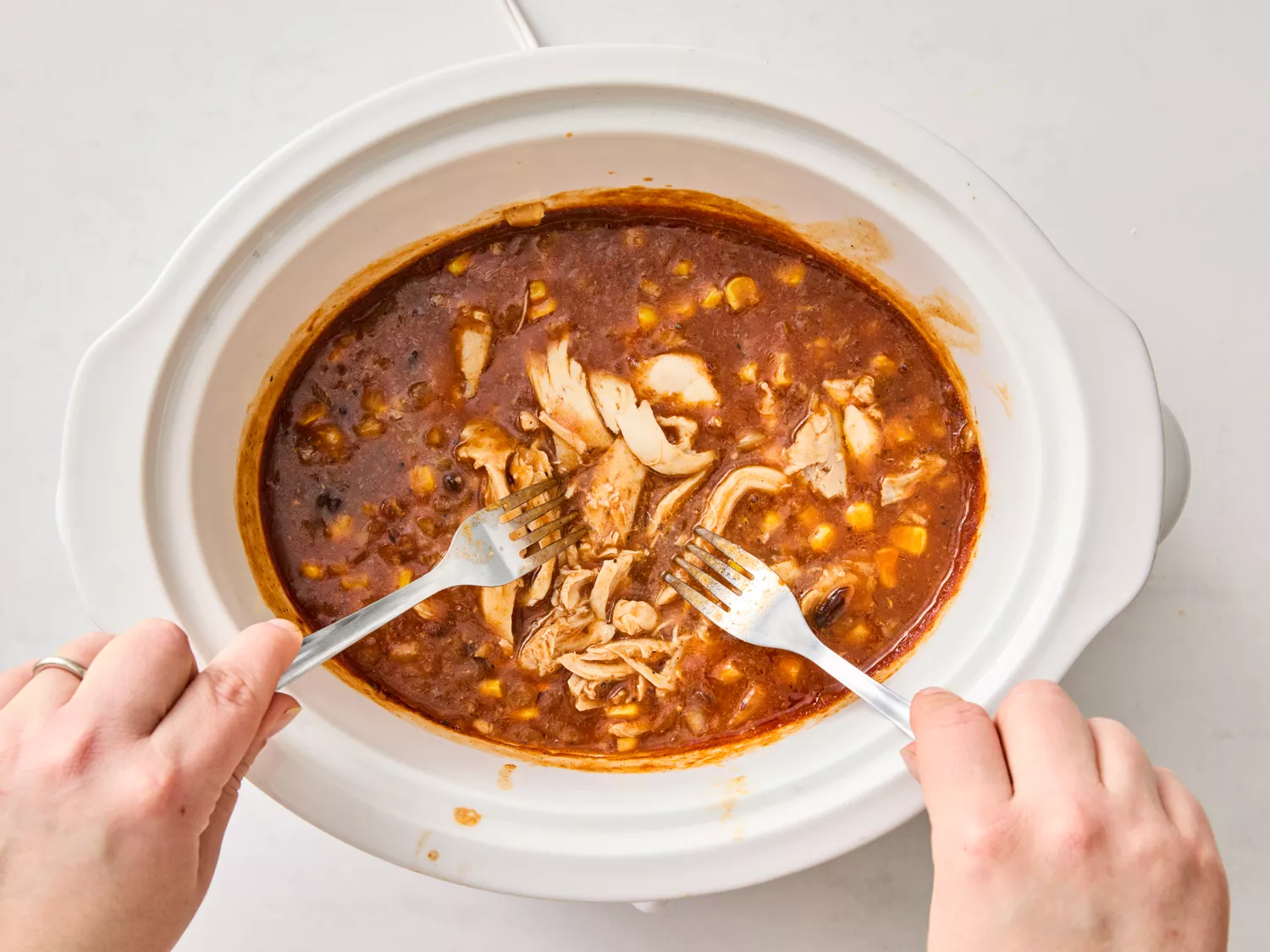 Chicken being shredded with forks inside the slow cooker
