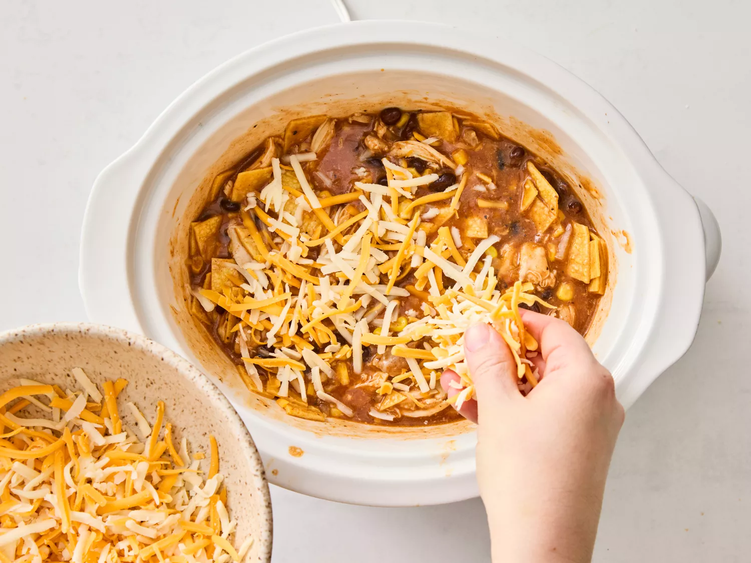 Cheese being sprinkled over the chicken enchilada mixture in the slow cooker
