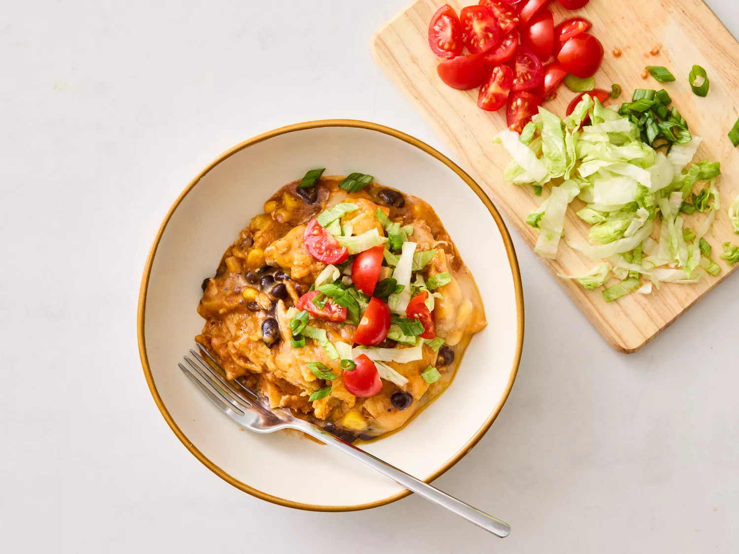 A bowl of chicken enchilada casserole garnished with lettuce and tomatoes