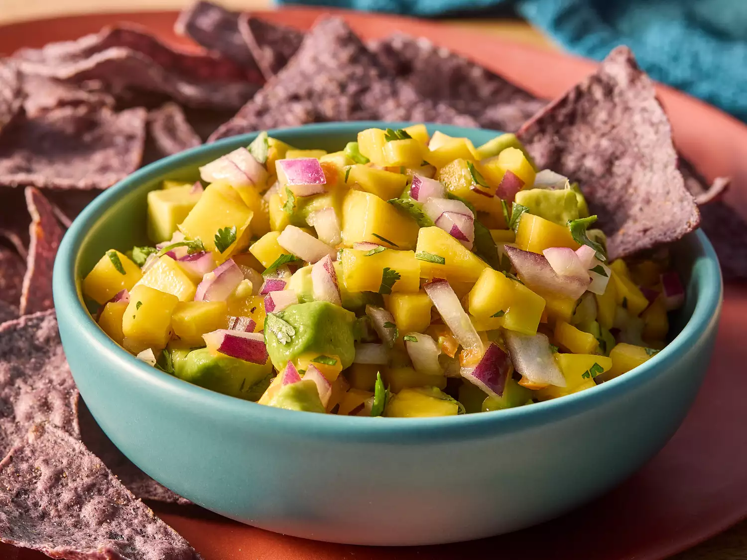 Close up of mango avocado salsa garnished with cilantro in a blue bowl with blue corn chips
