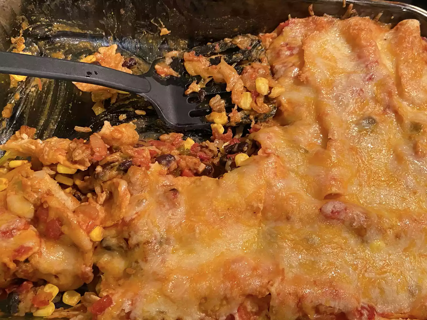 Close up view of black bean and rice enchiladas in a glass baking dish with a black spatula