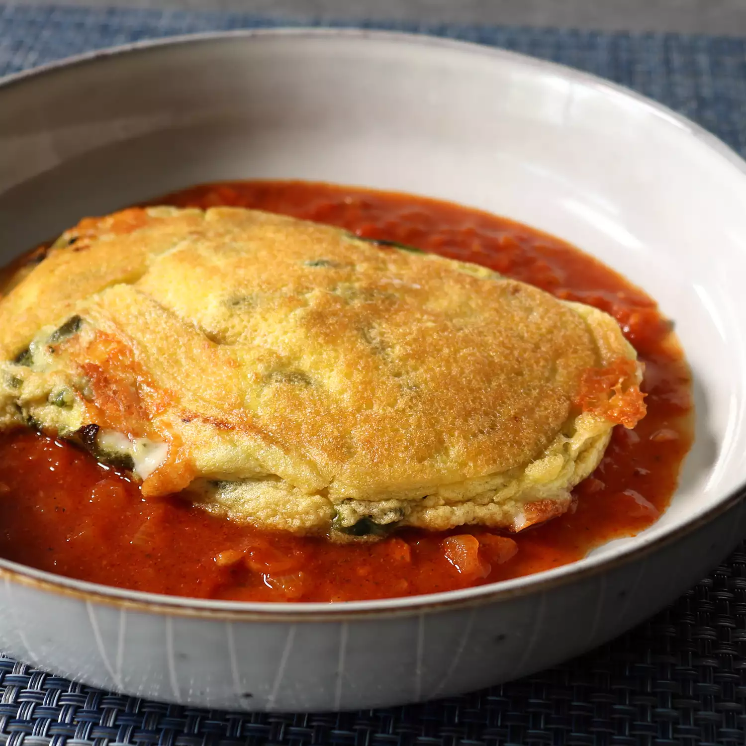 close up view of a Chile Relleno Pancake over red sauce in a bowl