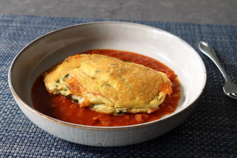 A bowl holding a pancake version of chile relleno on a spiced tomato sauce