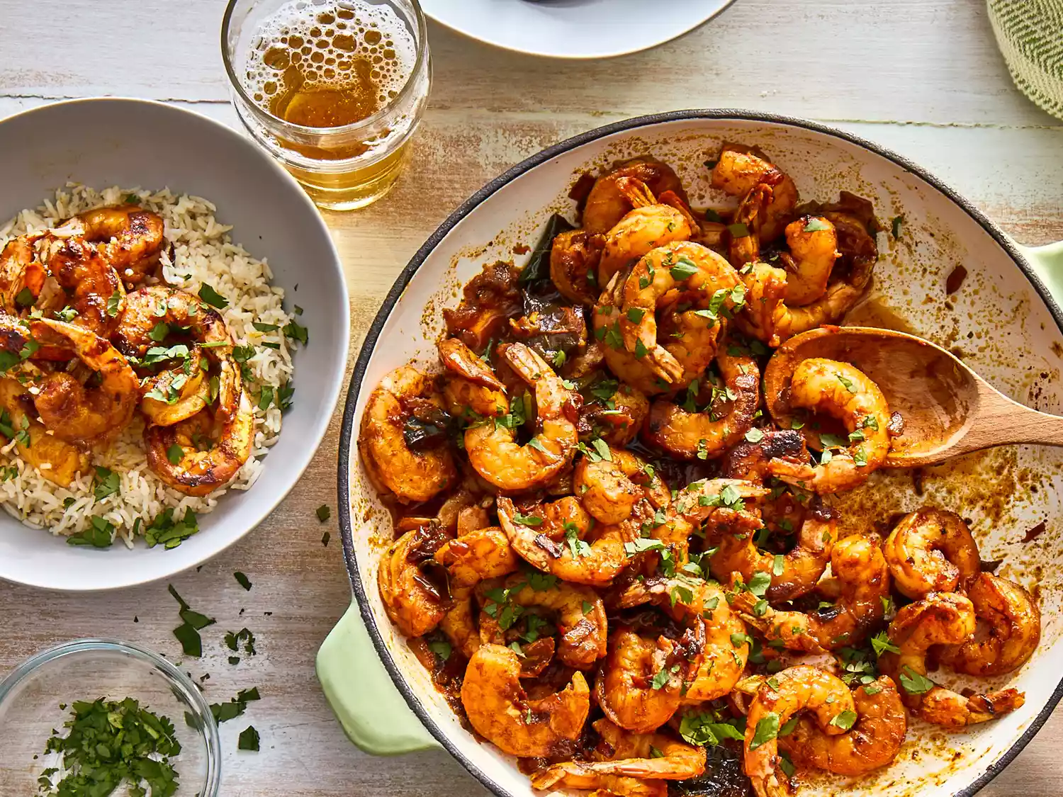 Close up view of shrimp curry in a pan with a wooden spoon, and shrimp curry over rice in a bowl