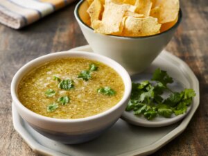 Mid angle looking at a bowl of tomatillo salsa verde and a side of tortilla chips