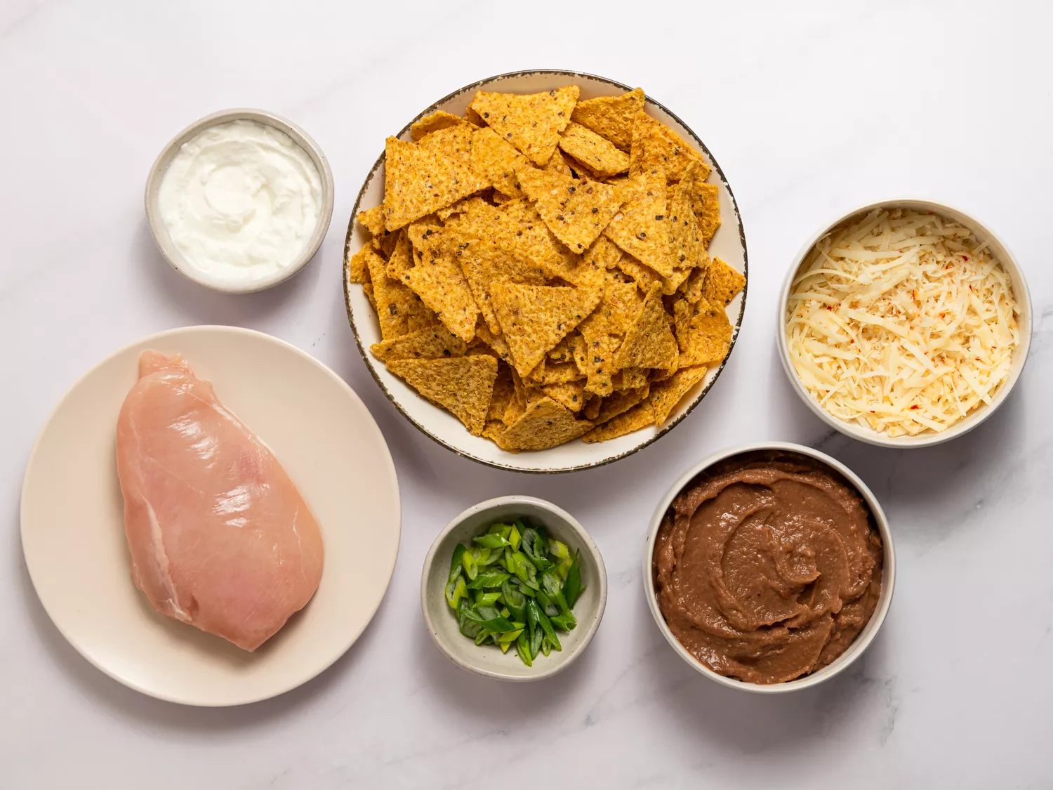 Ingredients for nachos including chicken, cheese, chips, and beans.