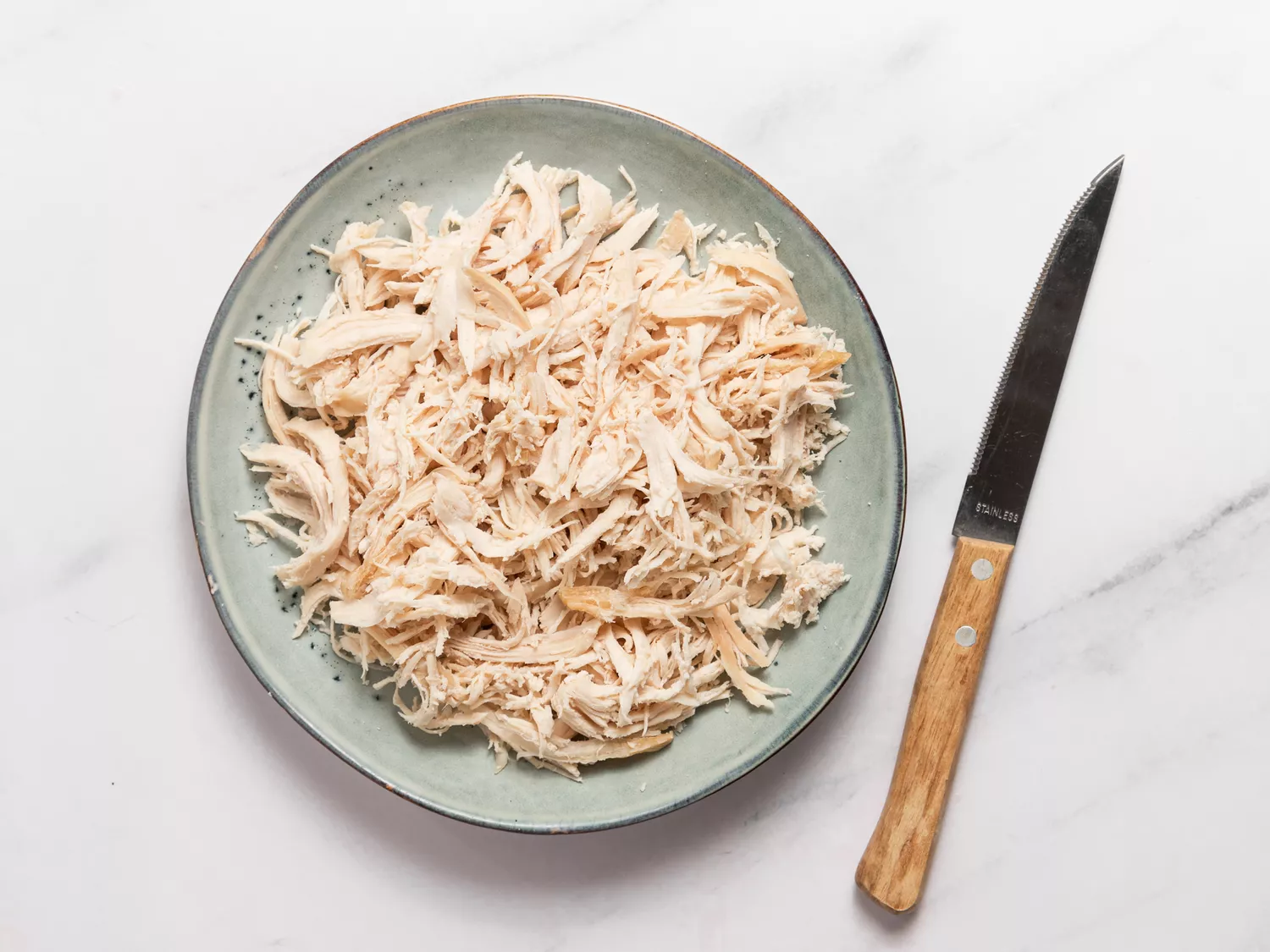 Shredded cooked chicken on a plate with a knife beside it.