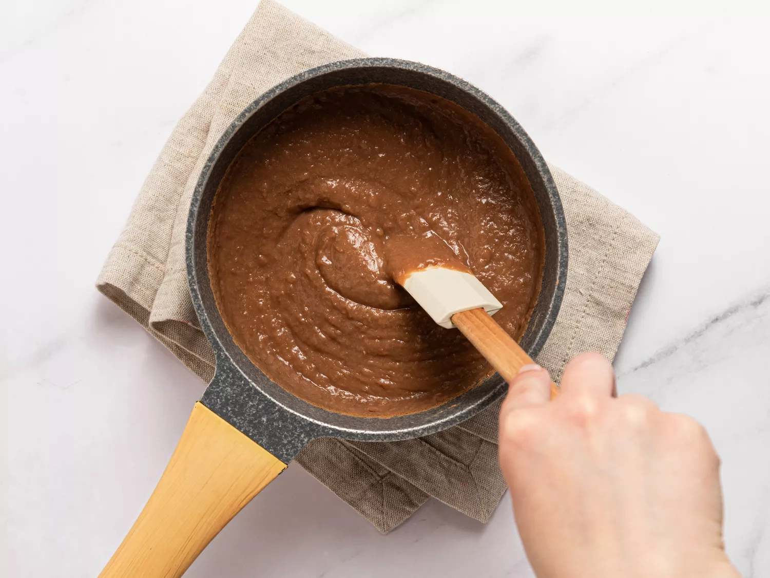 Refried beans being stirred in a saucepan with a spatula.