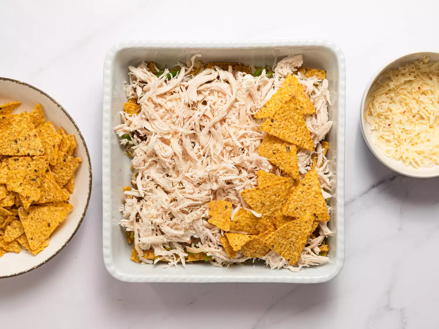 Layering shredded chicken and tortilla chips in a baking dish.