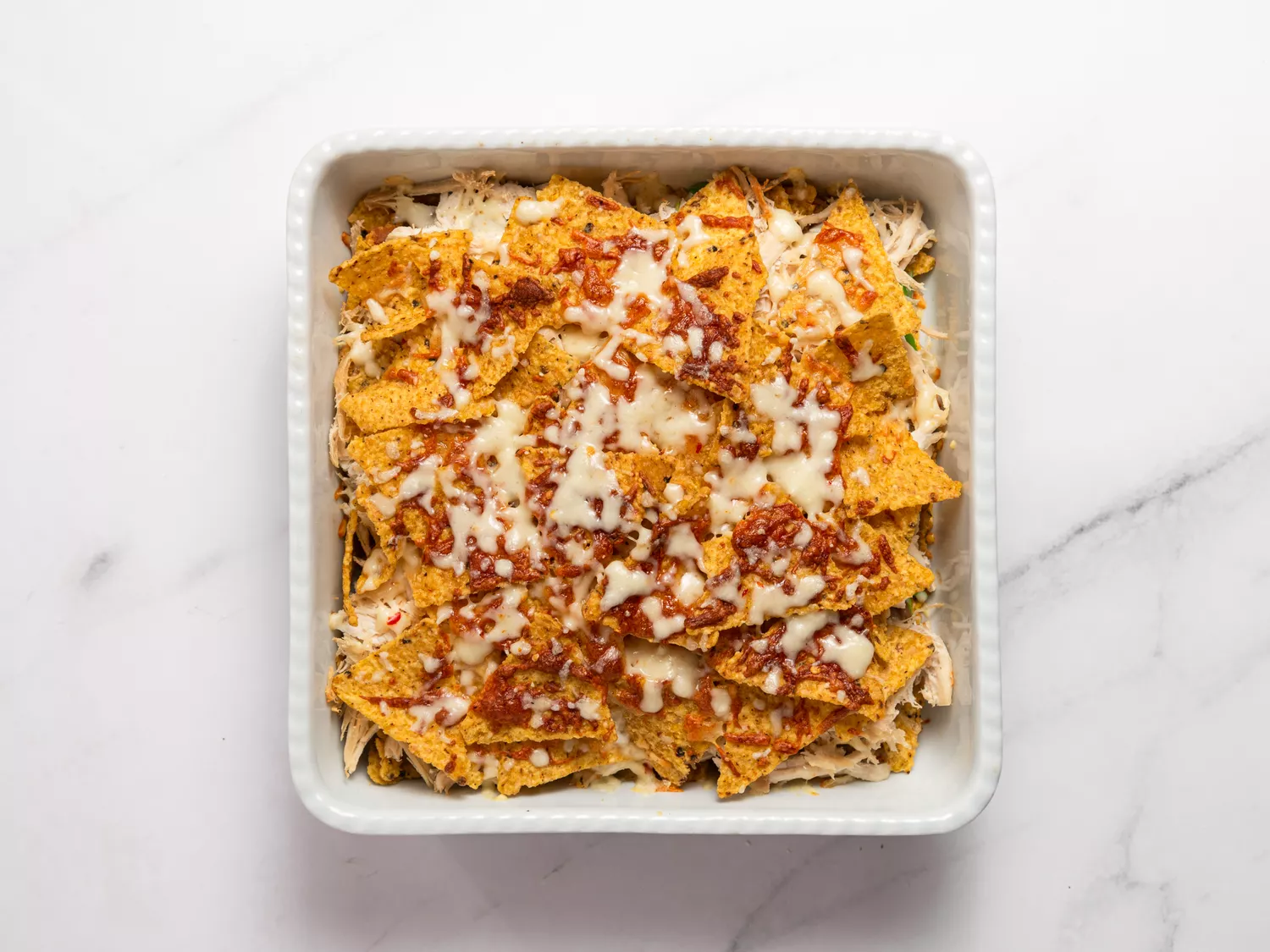 Unbaked nachos with cheese, chicken, and sauce in a dish.