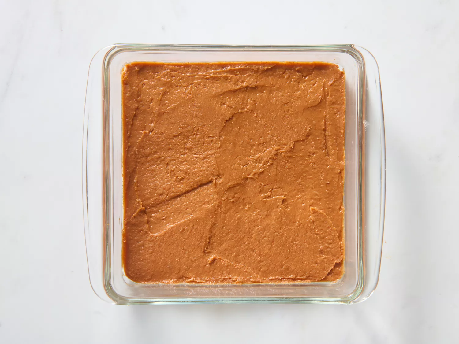 A glass dish with a layer of seasoned refried beans