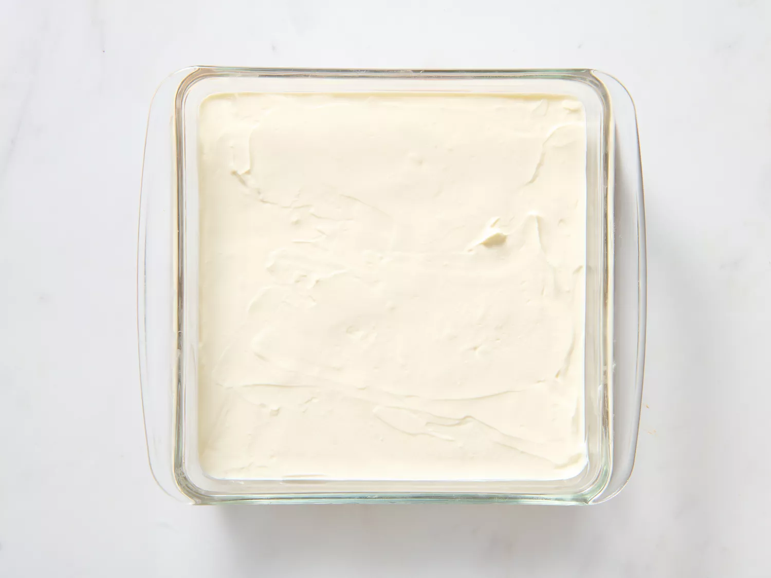 A glass baking dish with sour cream and cream cheese mixture layered on top of refried beans