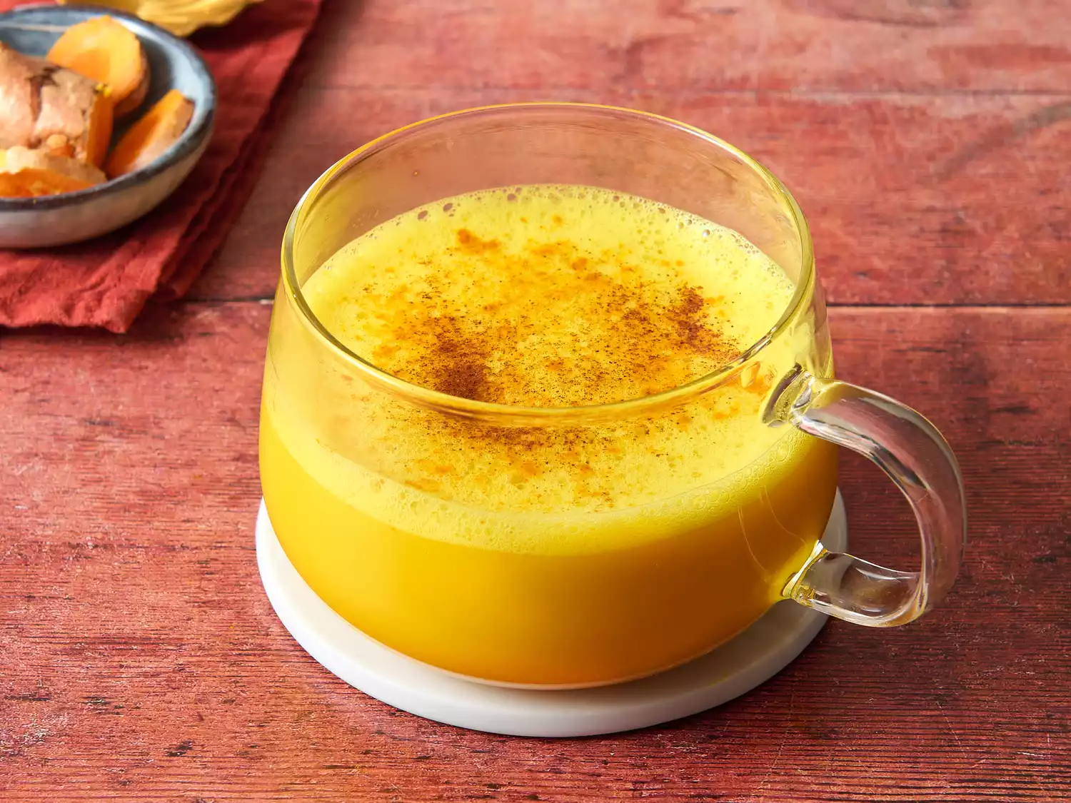 Glass mug of golden turmeric latte with cinnamon on wooden table.