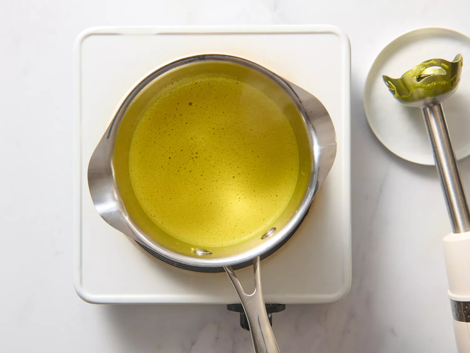 Saucepan with blended turmeric latte and immersion blender on the side.