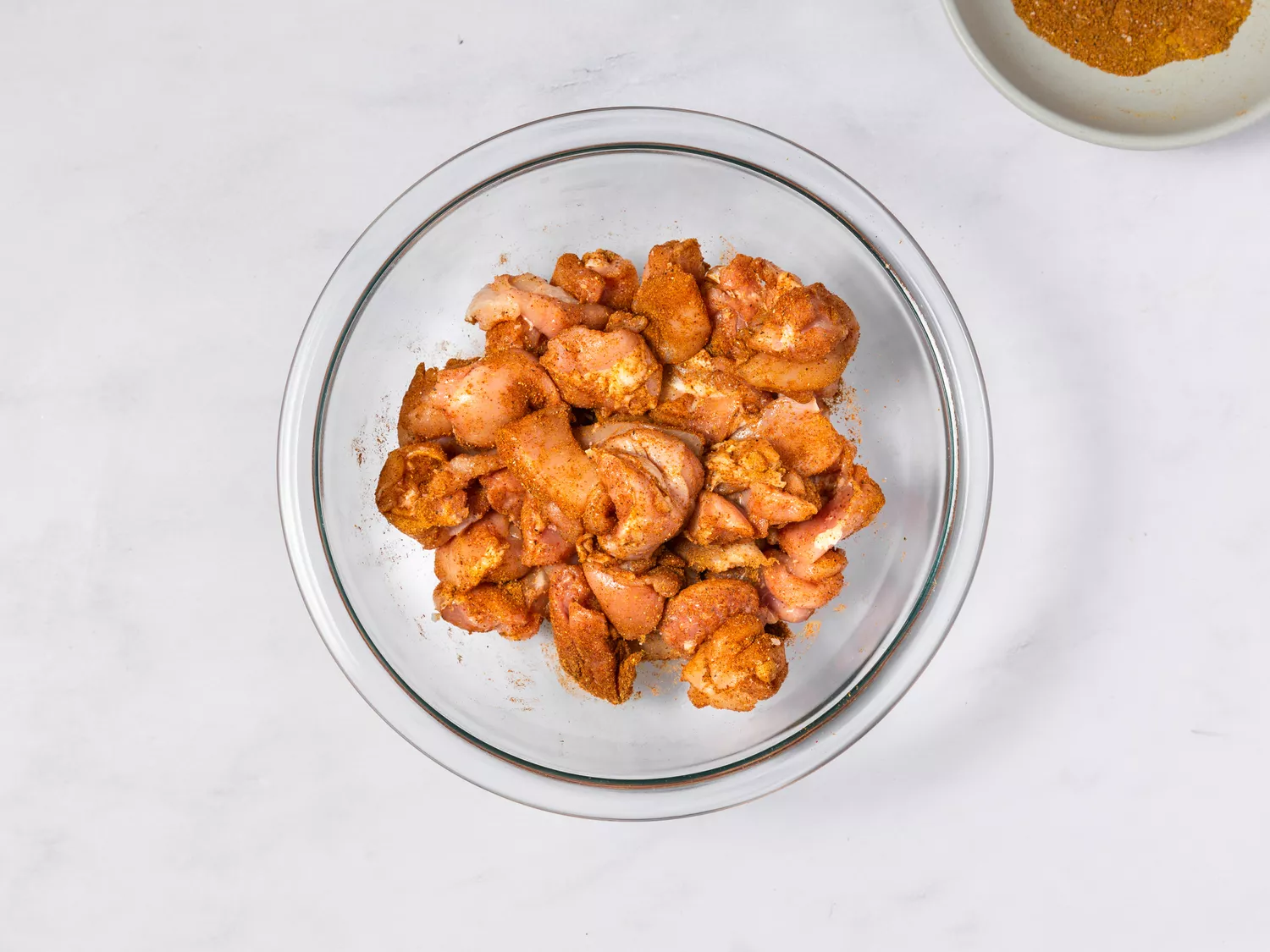 Raw chicken pieces seasoned with spices in glass bowl.