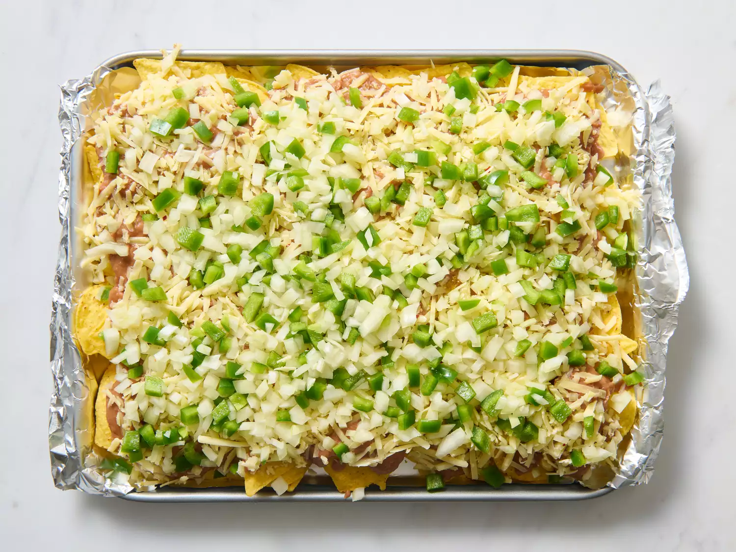 Unbaked nachos with cheese, beans, and vegetables.