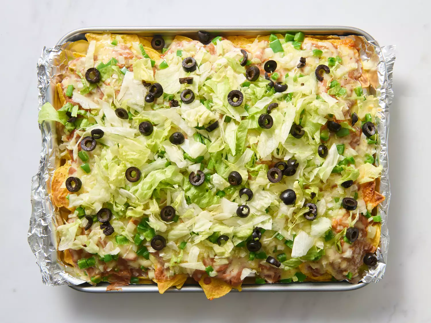 Baked nachos with melted cheese, lettuce, and olives.