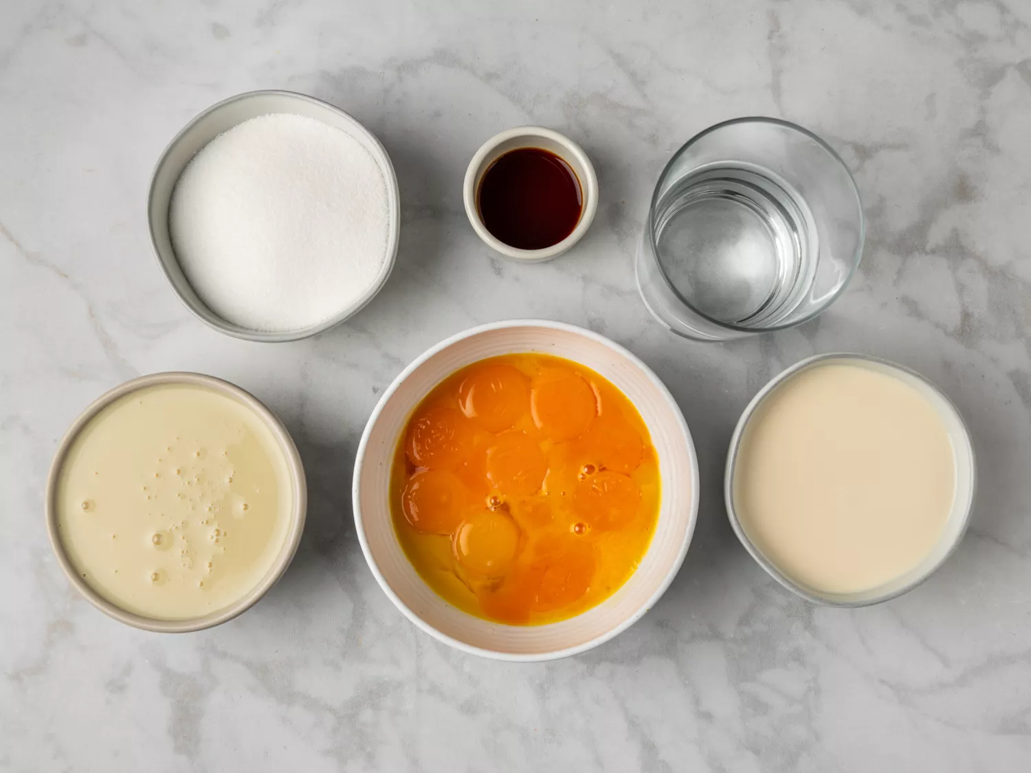 Ingredients for flan arranged on a marble surface.