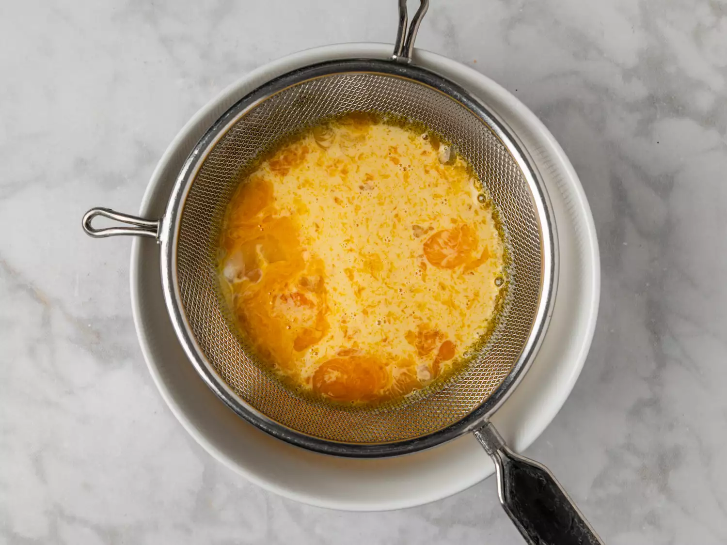 Egg mixture being strained through a fine mesh sieve.