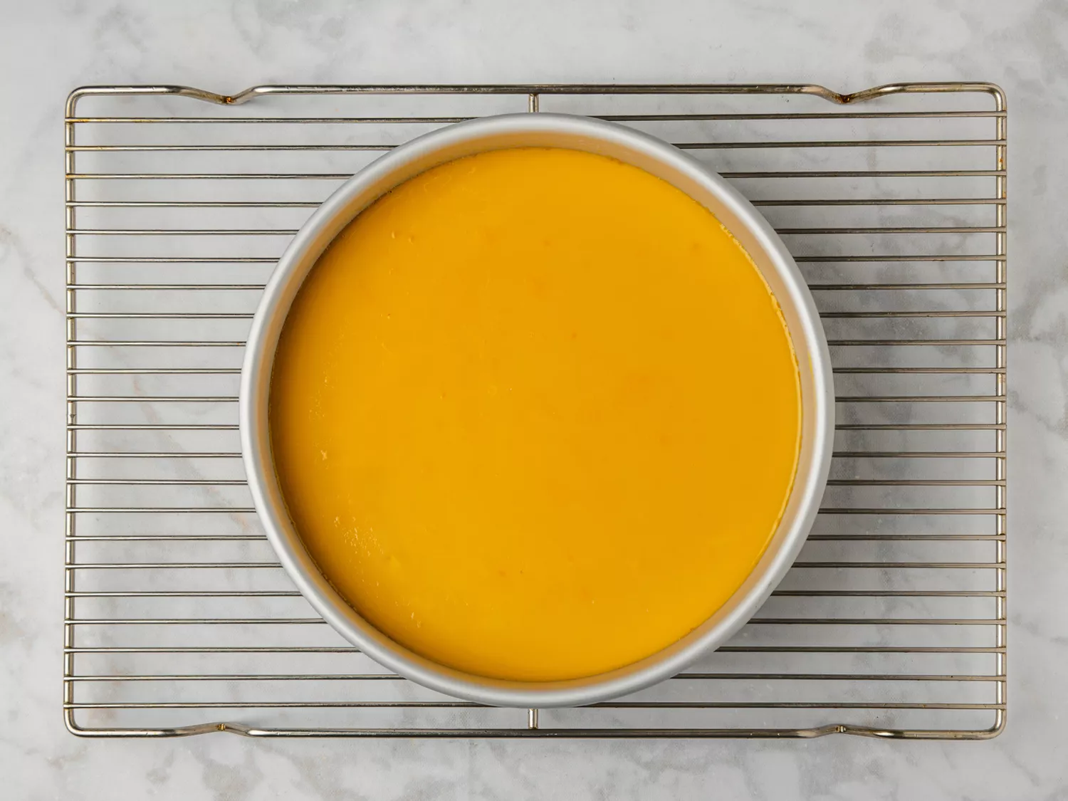 Baked flan cooling in a round pan on a wire rack.